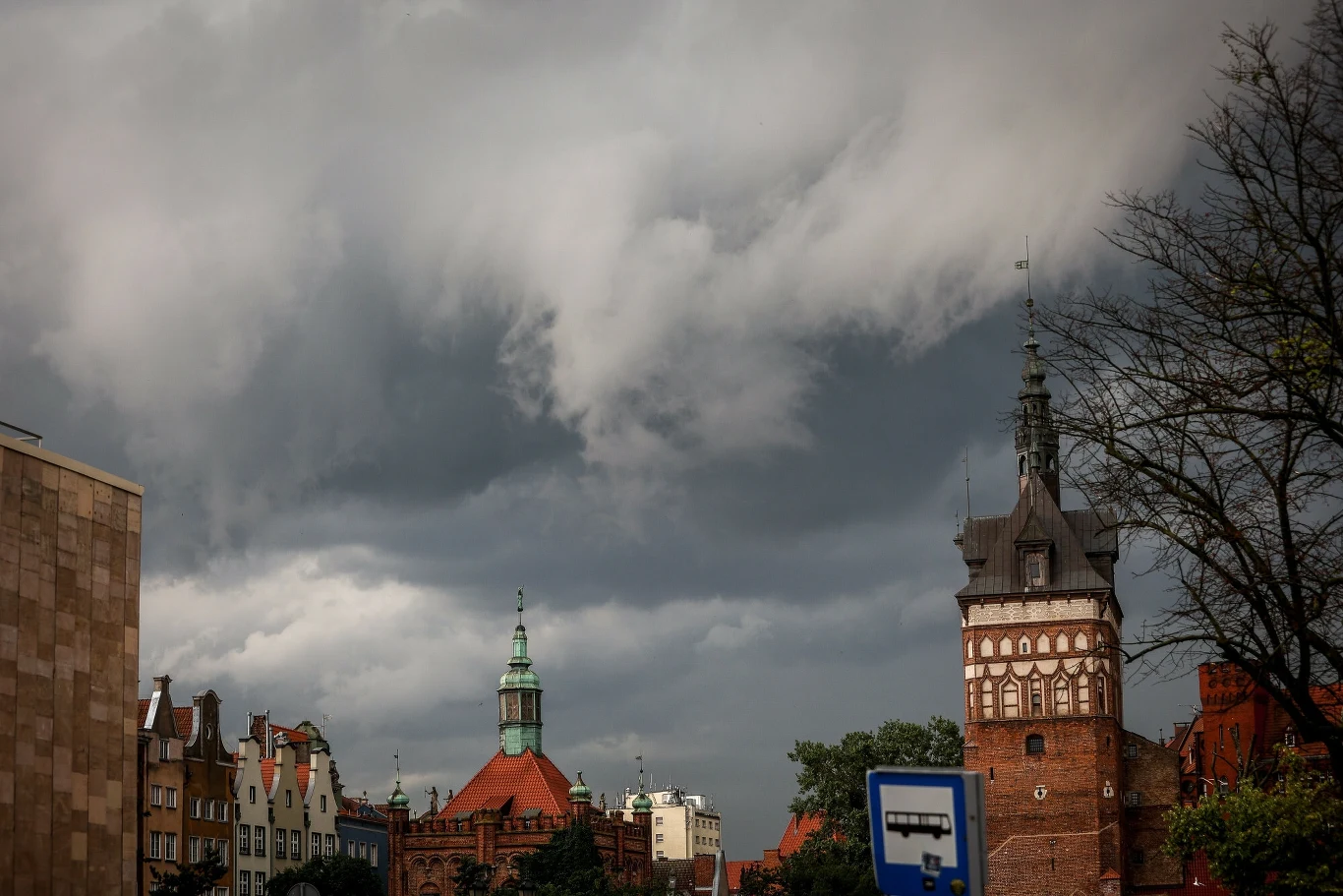 Prognoza pogody. IMGW wydało ostrzeżenia przed burzami Widok na historyczne budowle miasta pod ciężkimi, burzowymi chmurami. Na pierwszym planie zabytkowe kamienice oraz wieża kościelna. Zachmurzone niebo nadaje scenerii dramatyzmu.