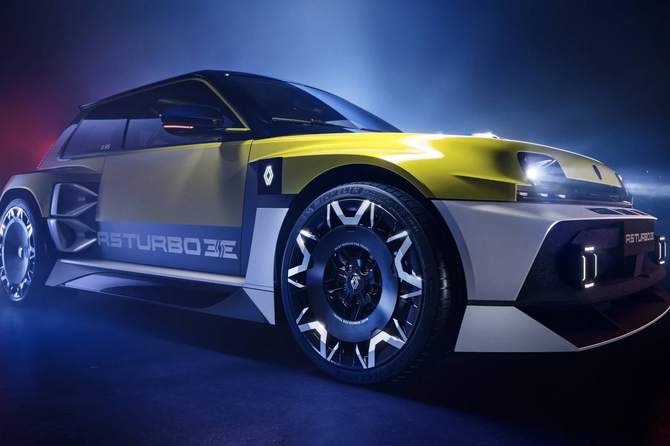 Renault 5 Turbo 3E oferuje 540 KM i 4,8 tys. Nm momentu obrotowego. Sportowy samochód w nowoczesnym, dynamicznym oświetleniu. Jaskrawa karoseria ozdobiona napisami „TURBO”.