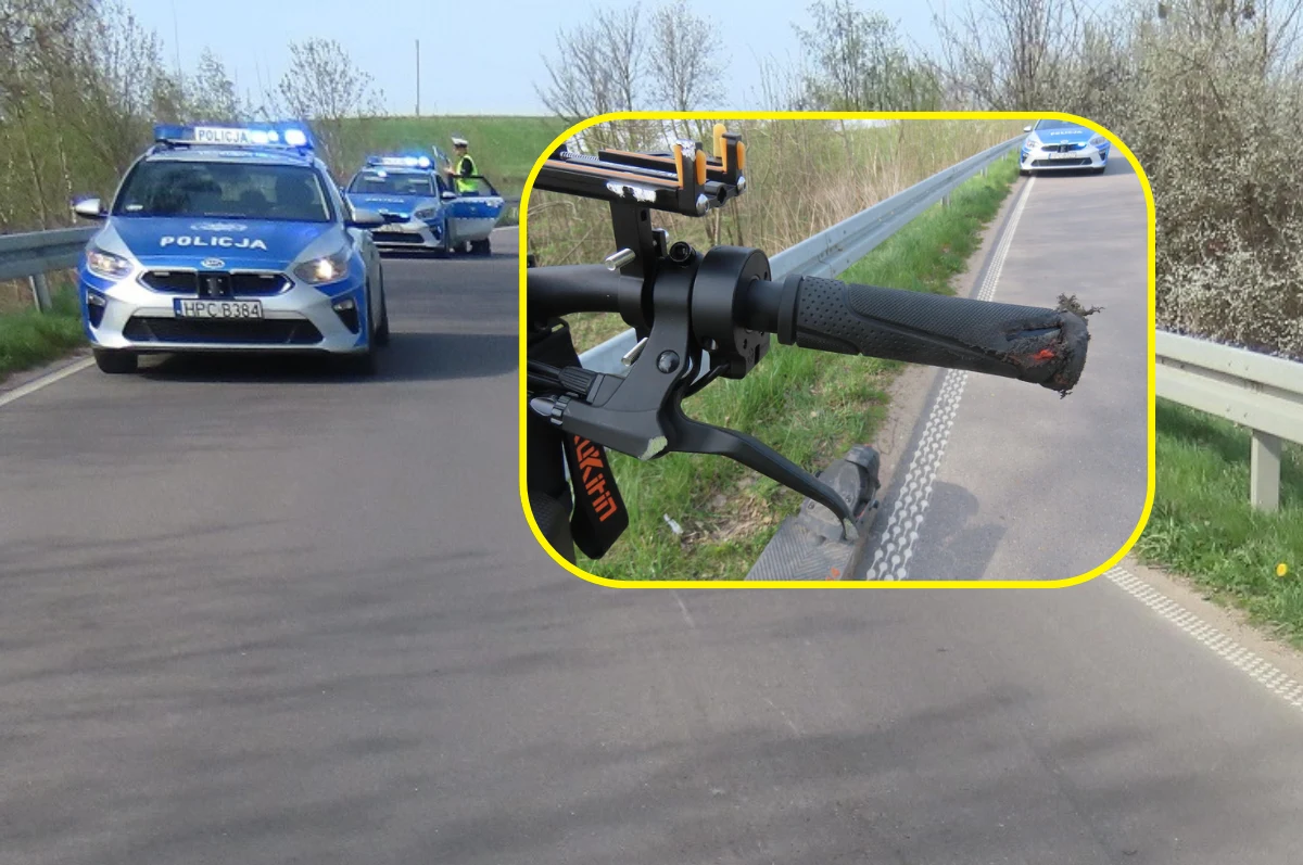 15-latek z 17-latką jechali hulajnogą elektryczną. Jak się okazało - bez kasków i z nadmierną prędkością. Auto policyjne na drodze z włączonymi światłami sygnalizacyjnymi, na poboczu widoczny motocykl z uchwytem kierownicy. W tle krajobraz z drzewami.