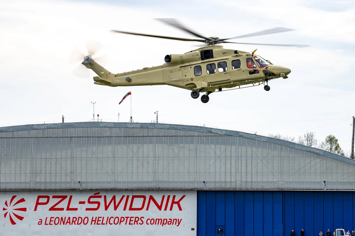 AW149 ze Świdnika odbył swój pierwszy lot. Ogromny sukces polskiej zbrojeniówki Helikopter wojskowy w locie nad halą produkcyjną PZL-Świdnik, firmą należącą do Leonardo Helicopters. Budynek z dużym logotypem na froncie i otoczenie przemysłowe w tle.