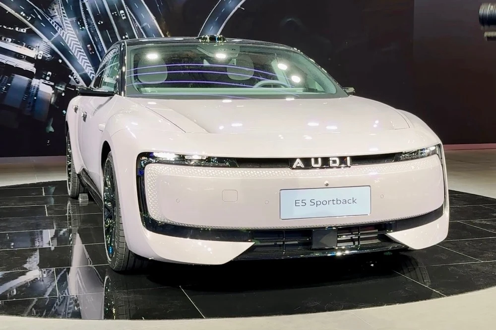 Samochód Audi E5 Sportback zaprezentowany na wystawie, uchwycony z przodu na ekskluzywnym tle. Elegancka, aerodynamiczna sylwetka i futurystyczne reflektory dominują w kadrze.
