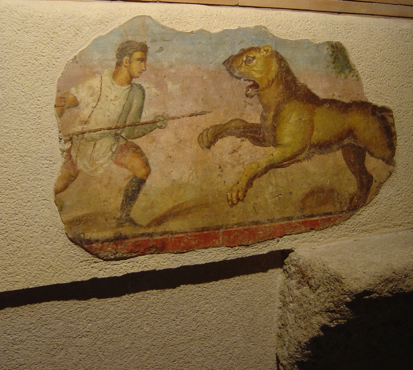 Starożytne malowidło przedstawiające człowieka z włócznią naprzeciw atakującego lwa, co obrazuje scenę walki między człowiekiem a dzikim zwierzęciem.