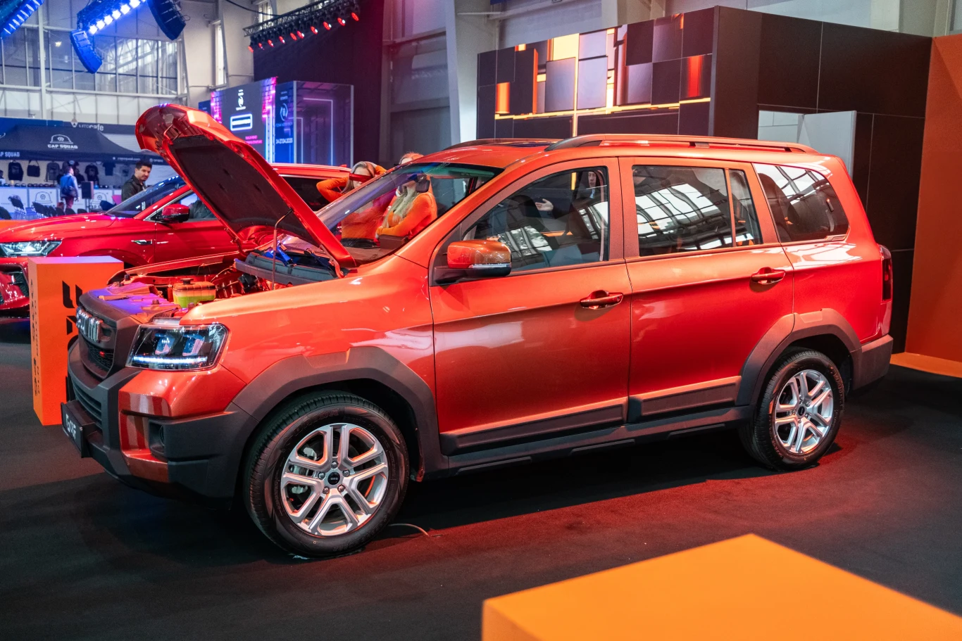 Czerwony samochód terenowy z otwartą maską wystawiony na ekspozycji w hali targowej. Nowoczesny design, reflektory w kształcie prostokąta i jaskrawy kolor przyciągają uwagę.