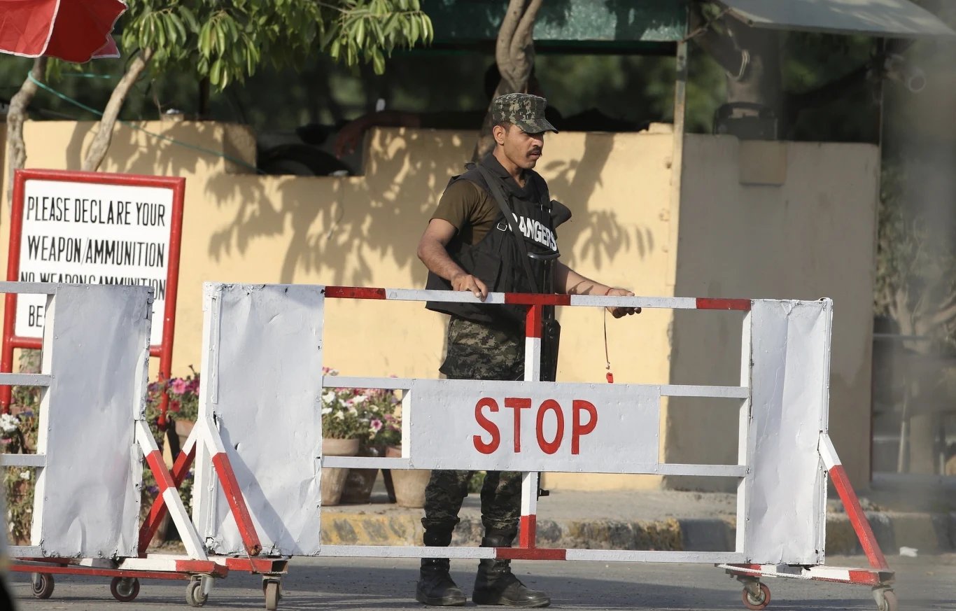 Napięcie na linii Indie-Pakistan. Islamabad ogłosił nową decyzję Żołnierz w mundurze stoi za metalową barierką z napisem "STOP", obok znaku przypominającego o zgłoszeniu posiadanej broni i amunicji. W tle widoczna jest roślinność oraz część budynku.