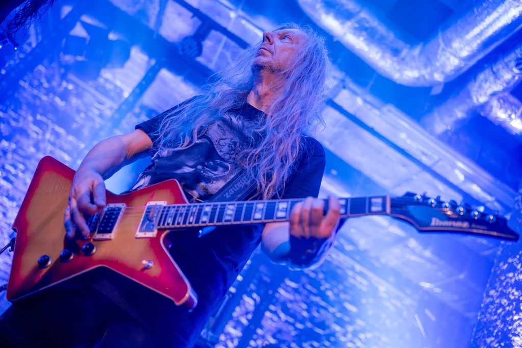Wojciech Hoffmann (Turbo) w Lublinie - 15 lutego 2025 r. Osoba z długimi blond włosami grająca na czerwonej gitarze elektrycznej, otoczona niebieskim oświetleniem scenicznym, z focusem na dynamiczną postawę i instrument muzyczny.