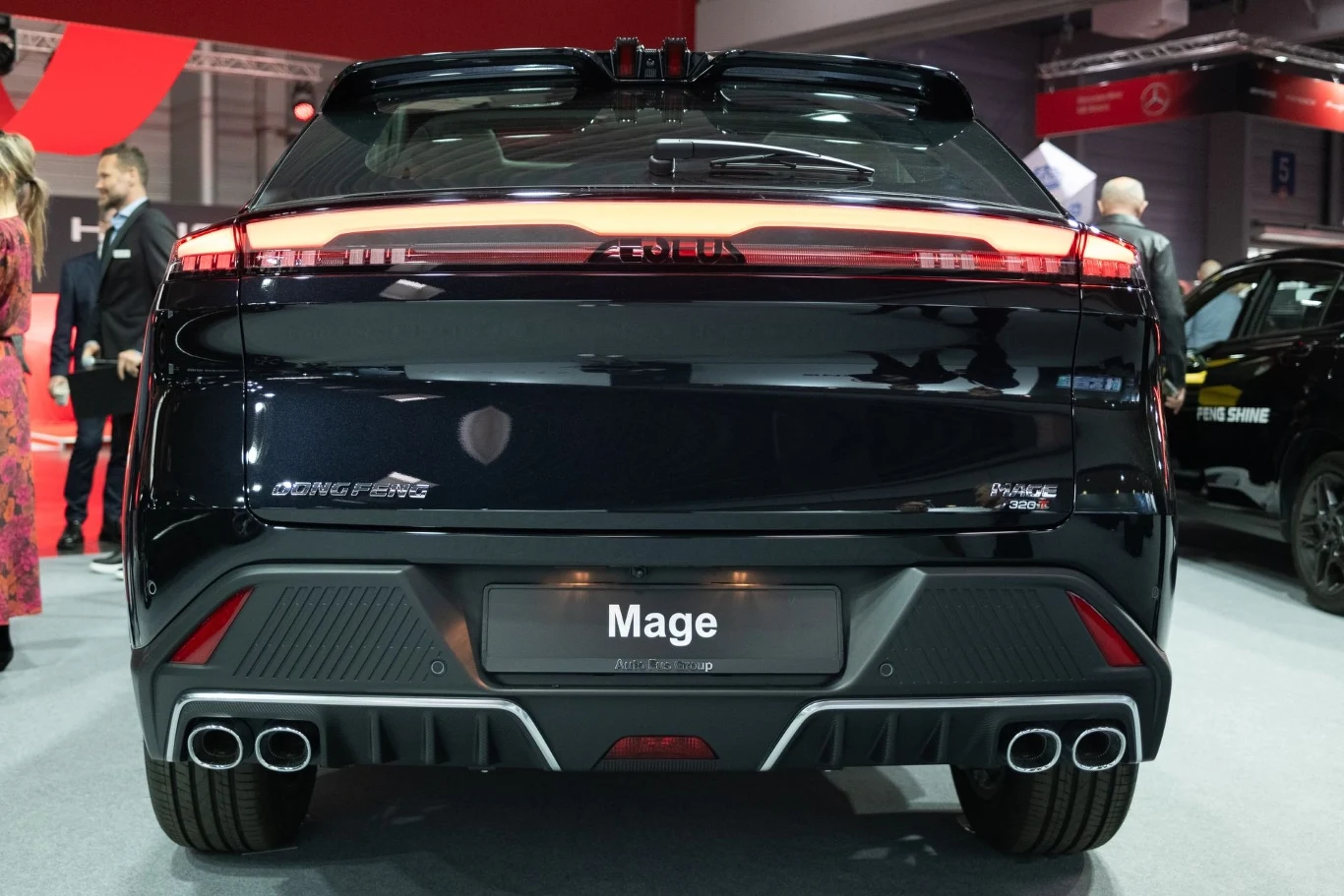 Widok z tyłu eleganckiego, nowoczesnego samochodu marki Mage, stojącego na wystawie motoryzacyjnej. Samochód wyróżnia się sportowym wyglądem z podwójnymi wydechami i nowoczesnym oświetleniem LED.