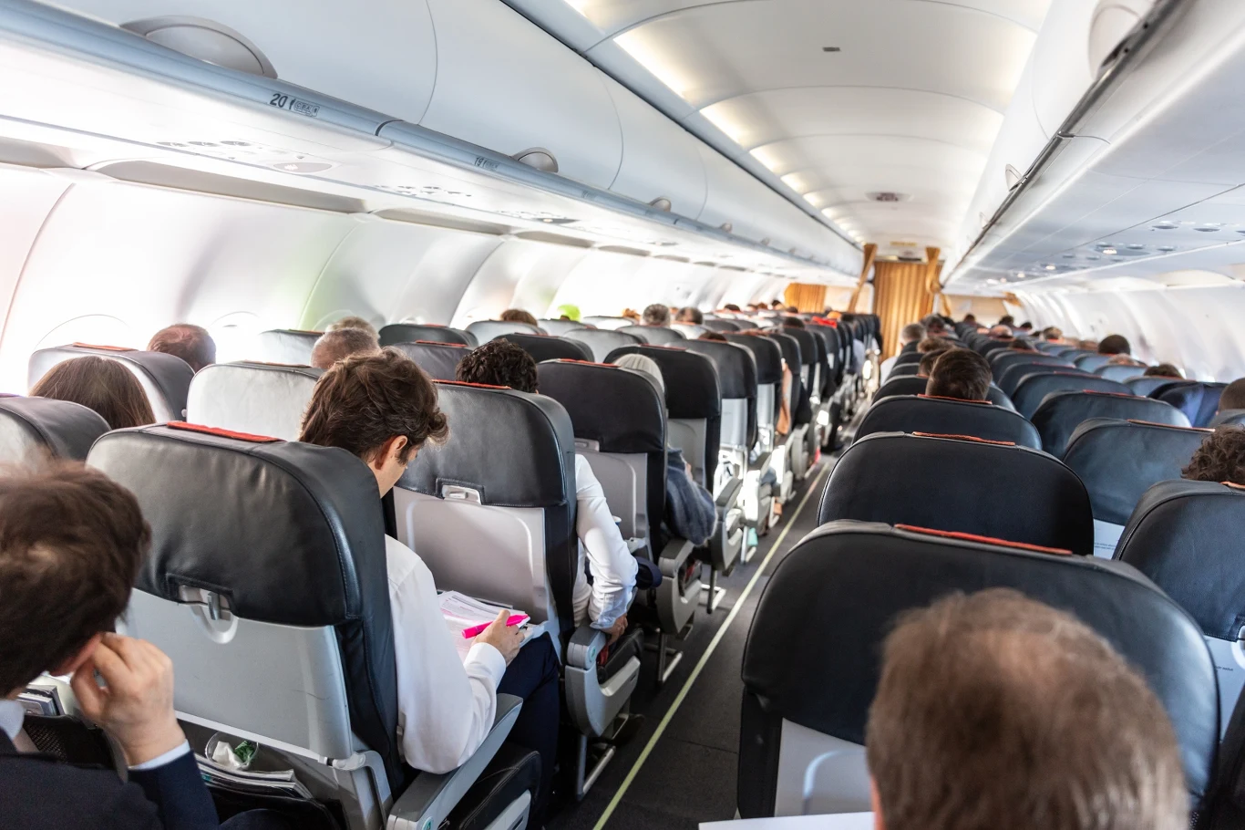 Pasażerowie mają dość płacenia za miejsca obok siebie Widok wnętrza samolotu pasażerskiego z siedzącymi pasażerami, rzędy siedzeń w środku, ludzie czytają lub odpoczywają.