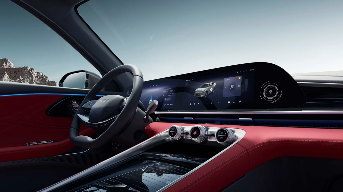 Wnętrze luksusowego samochodu z nowoczesnym cyfrowym kokpitem i dużym ekranem dotykowym na desce rozdzielczej. Wykończenie w kolorze czerwonym dodaje elegancji