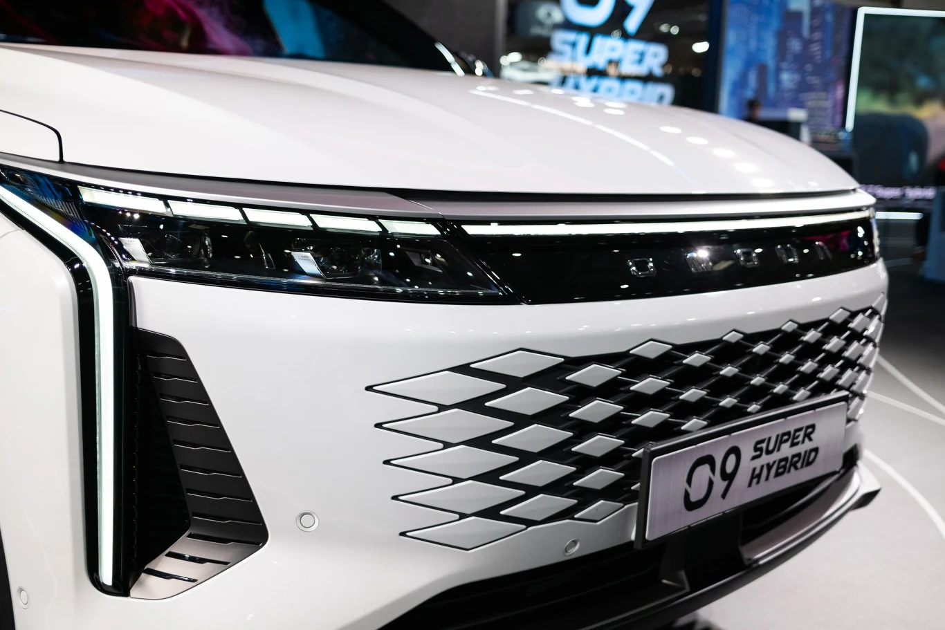 Przód białego samochodu z widocznym nowoczesnym grillem i reflektorami, tablica rejestracyjna wskazuje na model Super Hybrid.