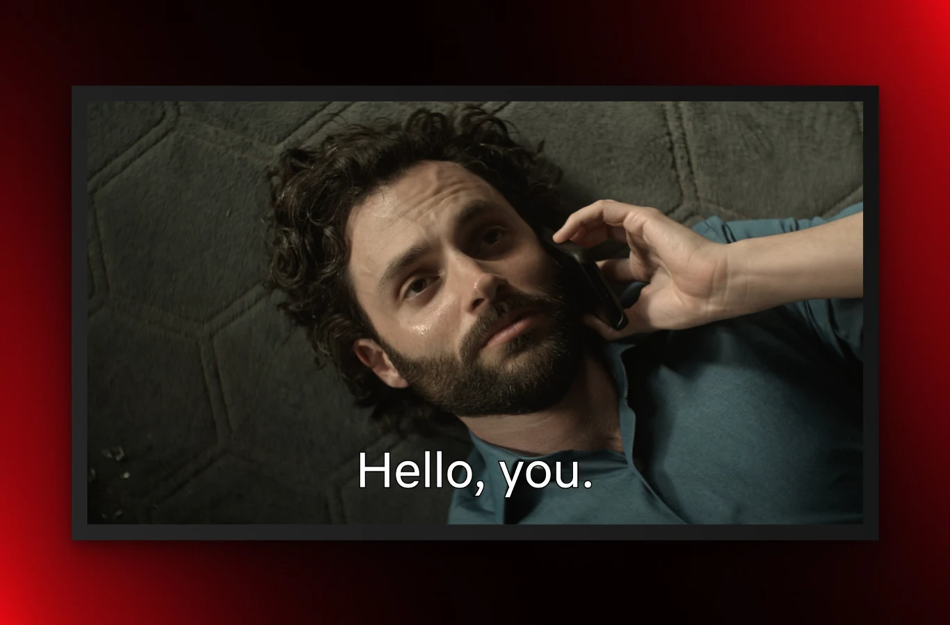 Netflix wprowadza nowe napisy. To wam się spodoba. Mężczyzna z brodą leżący na podłodze, patrzy w górę, trzymając telefon przy uchu. W tle znajduje się ciemne tło. Na obrazie widoczne są napisy 'Hello, you.'