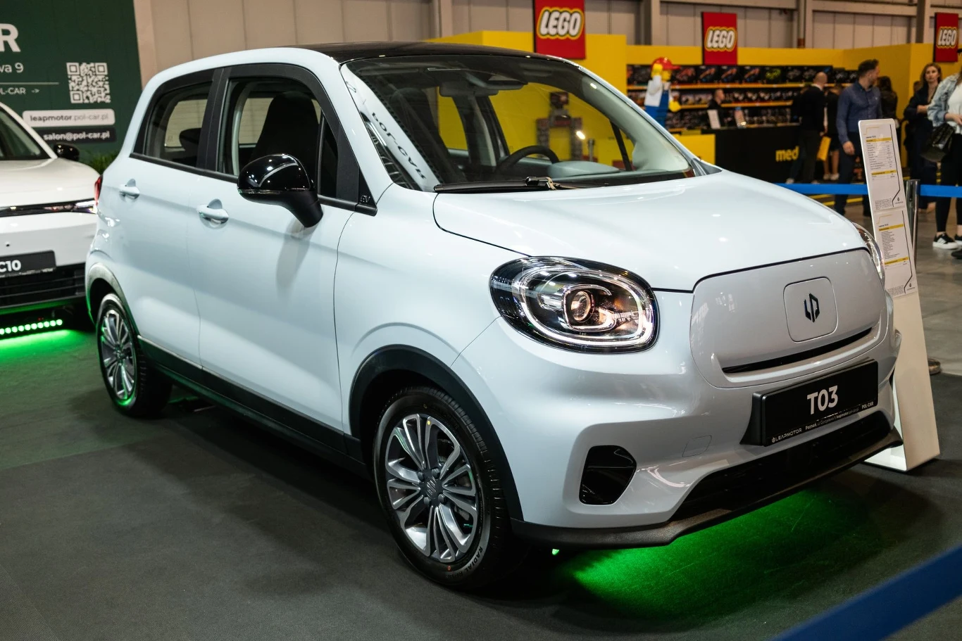 Producent wkroczył do Polski z modelem Leapmotor T03 Biały samochód elektryczny marki Leapmotor model T03 prezentowany na wystawie motoryzacyjnej, otoczony innymi stoiskami z produktami.