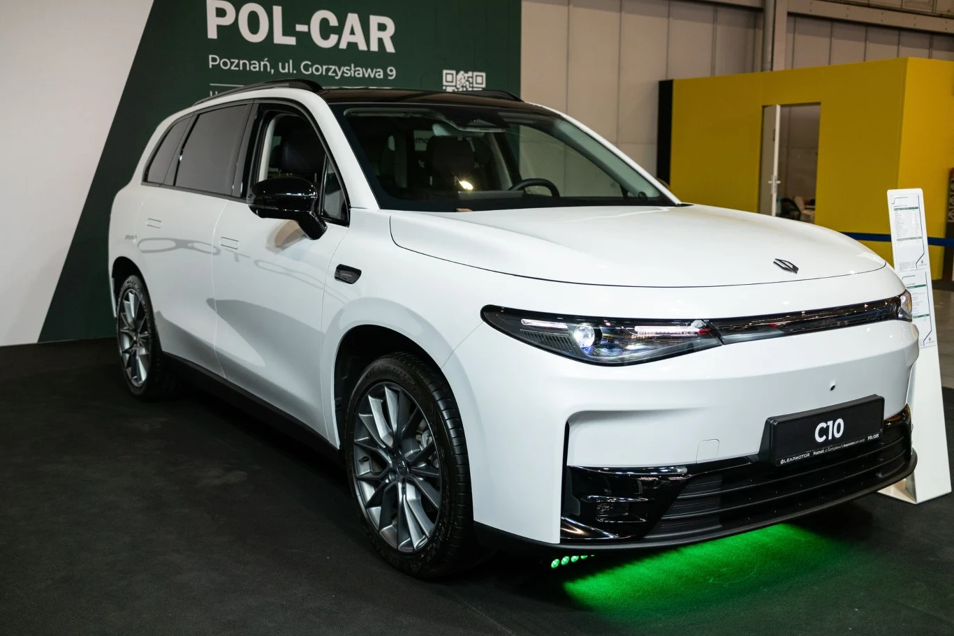 Leapmotor C10 również został zaprezentowany podczas targów. Biały samochód marki C10 zaprezentowany w salonie Pol-Car w Poznaniu. Auto stoi na ciemnym tle, podświetlone zielonym światłem od spodu. W tle tablica z nazwą salonu oraz żółty element konstrukcyjny.