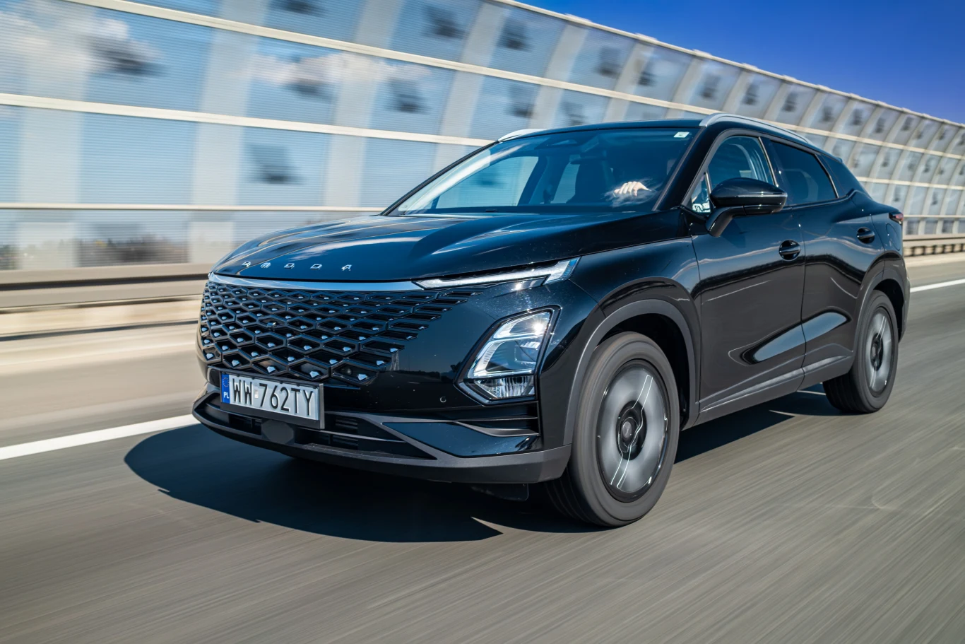 Czarny samochód osobowy jadący po autostradzie, na tle ekranów akustycznych. Widać jego dynamiczny kształt i nowoczesne linie nadwozia. Samochód ma polskie tablice rejestracyjne.