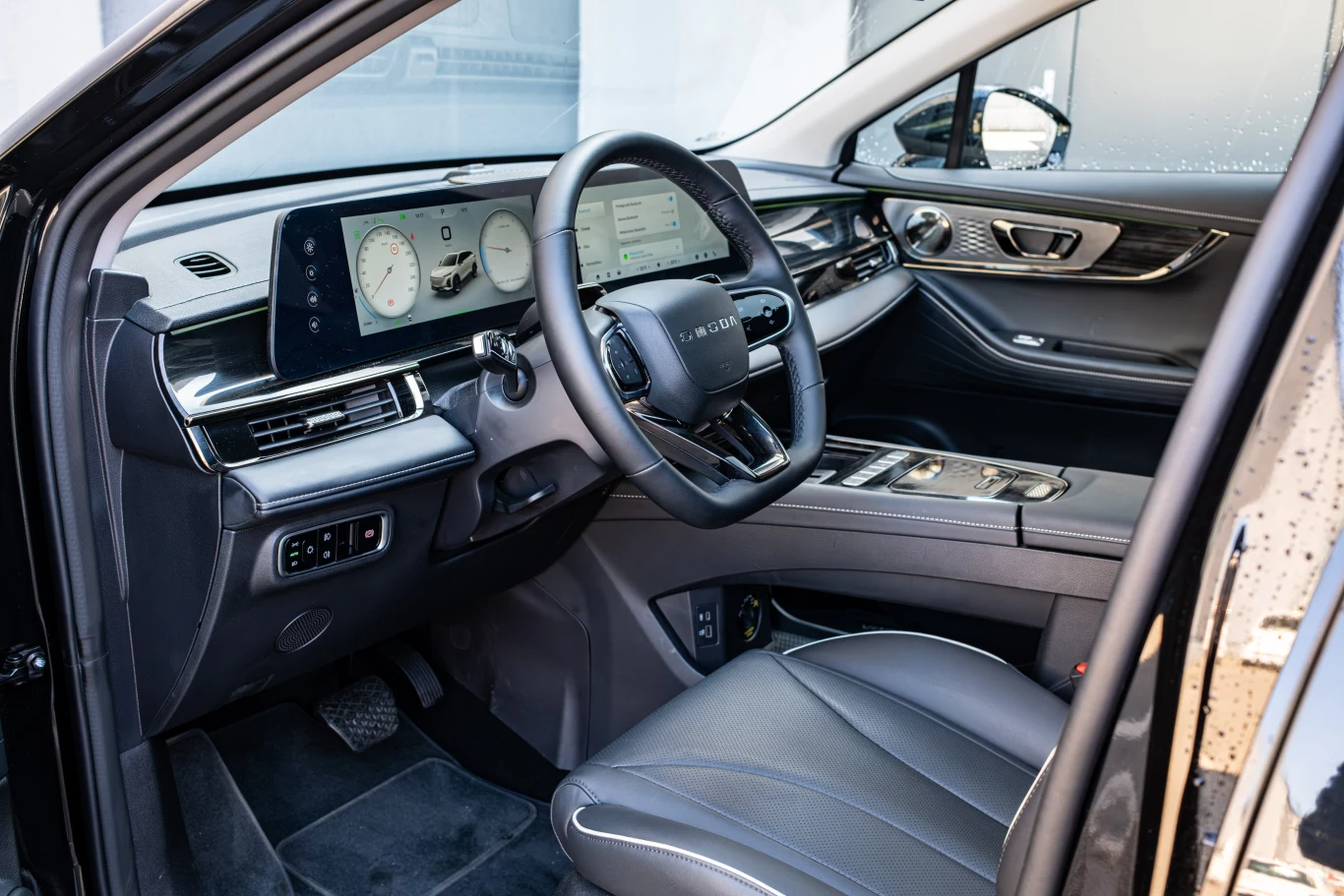 Wnętrze nowoczesnego samochodu elektrycznego z widocznym eleganckim kokpitem. Znajdują się tu cyfrowe zegary, duży ekran dotykowy oraz wielofunkcyjna kierownica. Fotele są wykończone skórą, a całość utrzymana w minimalistycznym stylu.