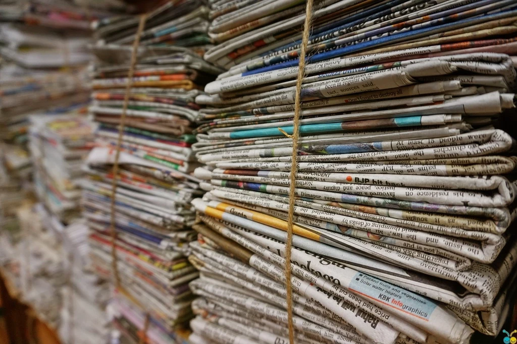 Fot. pixabay.com/congerdesign Stosy gazet ułożone w równych rzędach, związane sznurkiem, pokazujące ilość prasy i informacji drukowanej zbieranej na przestrzeni czasu.