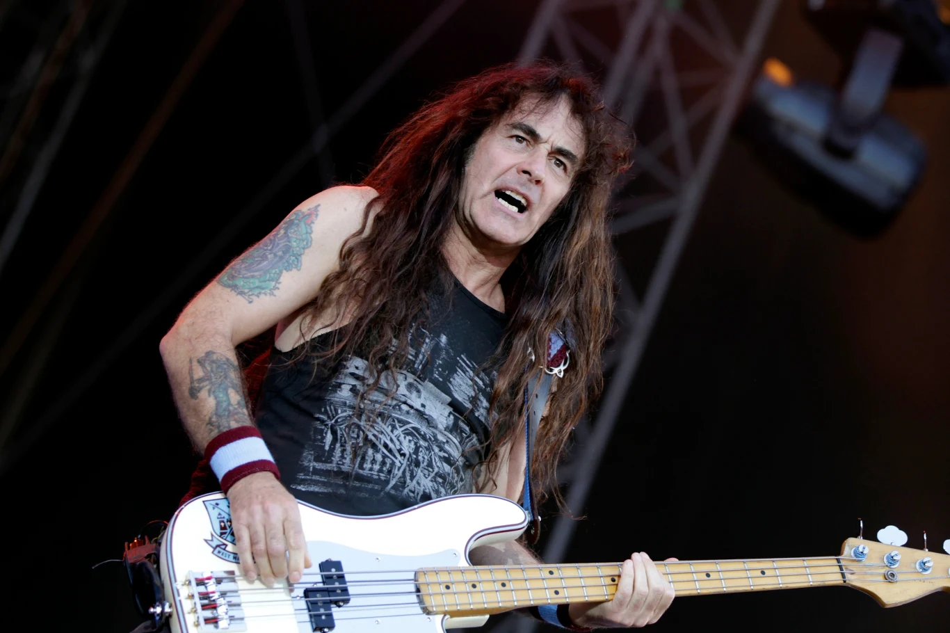 Basista zespołu Iron Maiden Muzyk grający na gitarze basowej podczas koncertu, dynamiczna postawa i wyraz twarzy podkreślają intensywność występu. W tle widoczne elementy sceniczne.