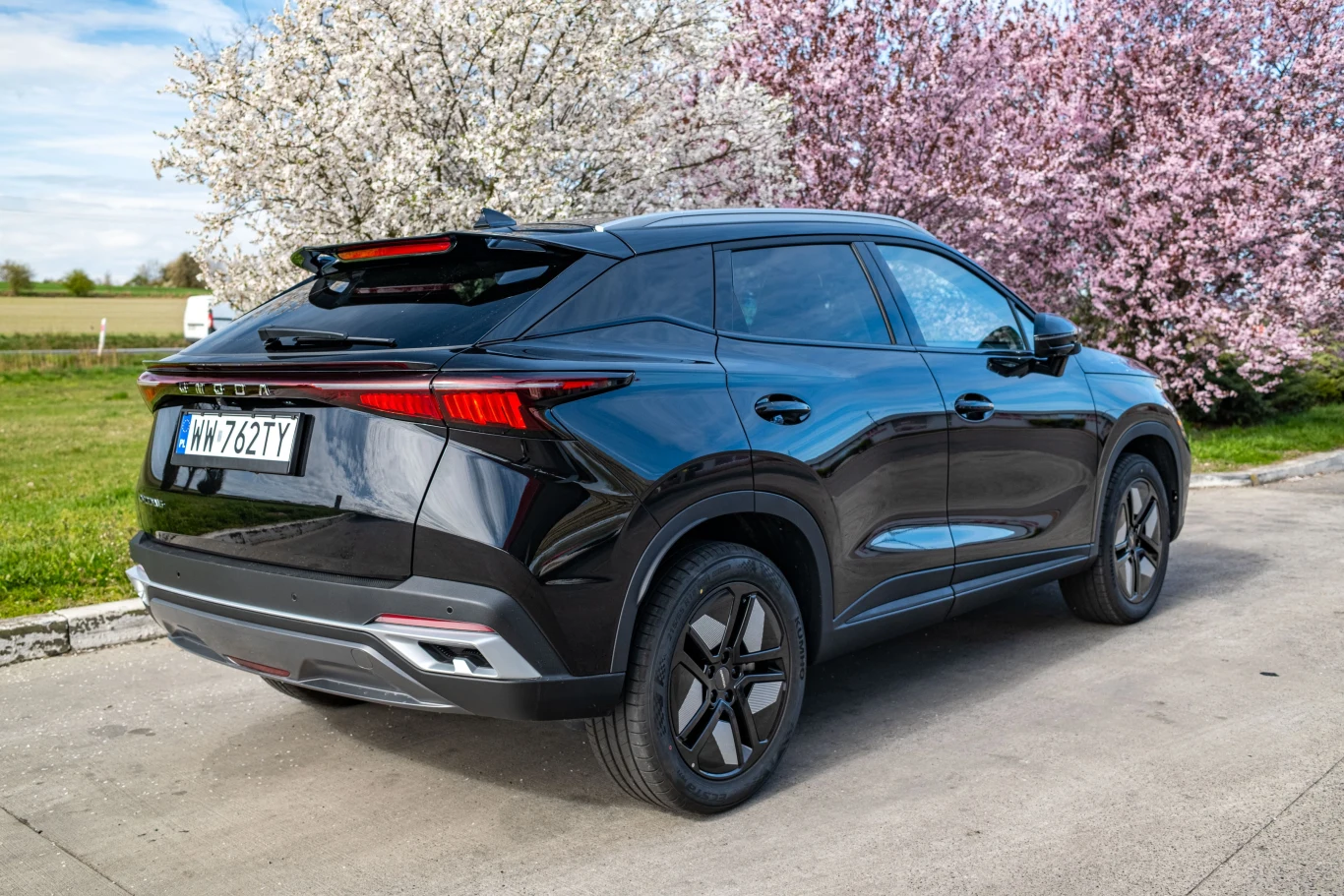 Czy w Omodzie trzeba wymienić olej po tysiącu km? Czarny samochód zaparkowany na tle kwitnących drzew, z widocznymi detalami tylnych świateł i eleganckim designem nadwozia.