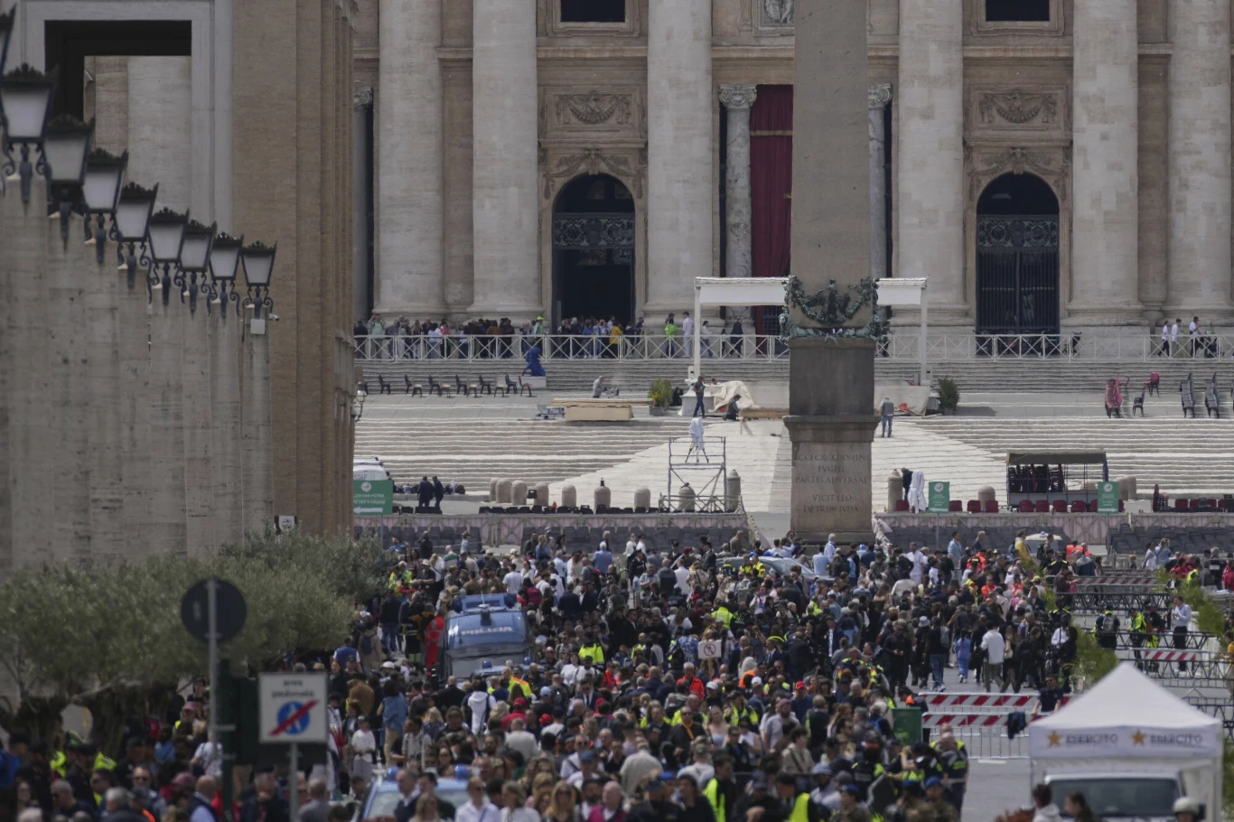 Trwają przygotowania do pogrzebu papieża Franciszka Tłum ludzi zgromadzony przed kolumnadą i budynkiem z wielkimi kolumnami. Widok przypomina plac przed historycznym budynkiem, a ludzie wydają się uczestniczyć w dużym wydarzeniu publicznym.