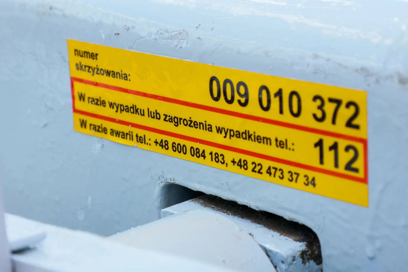 Naklejka PK potrafi uratować życie. Tabliczka informacyjna z numerami kontaktowymi na wypadek zagrożenia lub awarii. Widoczny jest numer skrzyżowania oraz numery telefonu.