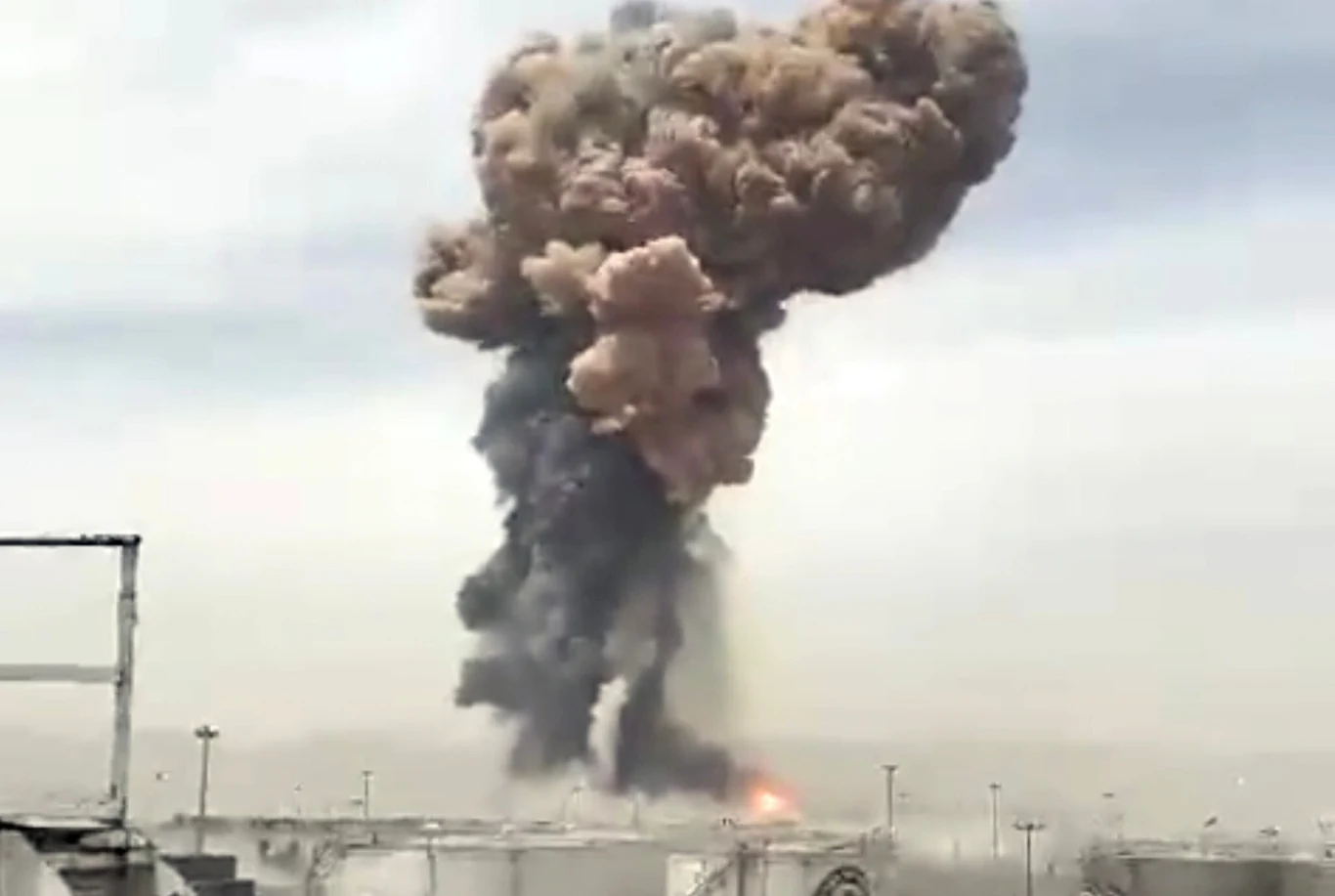 Eksplozja w porcie Szahid Radża'i w mieście Bandar-e Abbas Ogromna chmura dymu i pyłu unosząca się po wybuchu, widoczne płomienie u podstawy. W tle pochmurne niebo.