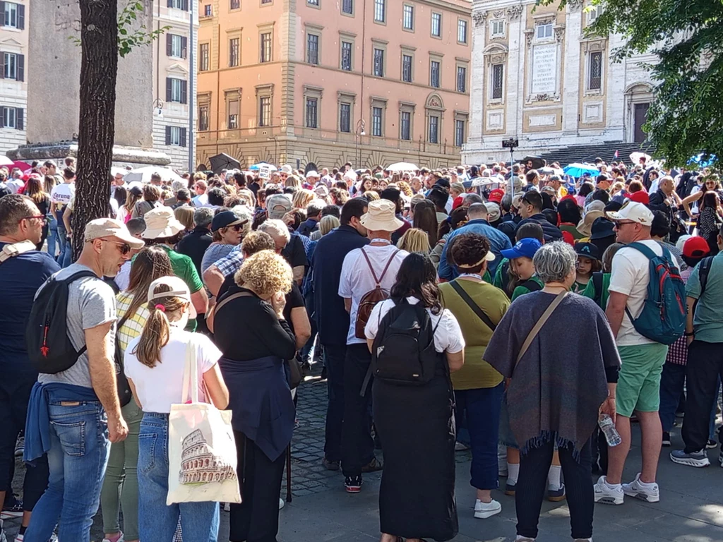 Oczekujący na wejście do bazyliki Tłum ludzi zgromadzonych na ulicy w centrum miasta, w tle widać historyczne budynki. Wszyscy skupieni na wydarzeniu, atmosfera napięcia i oczekiwania.