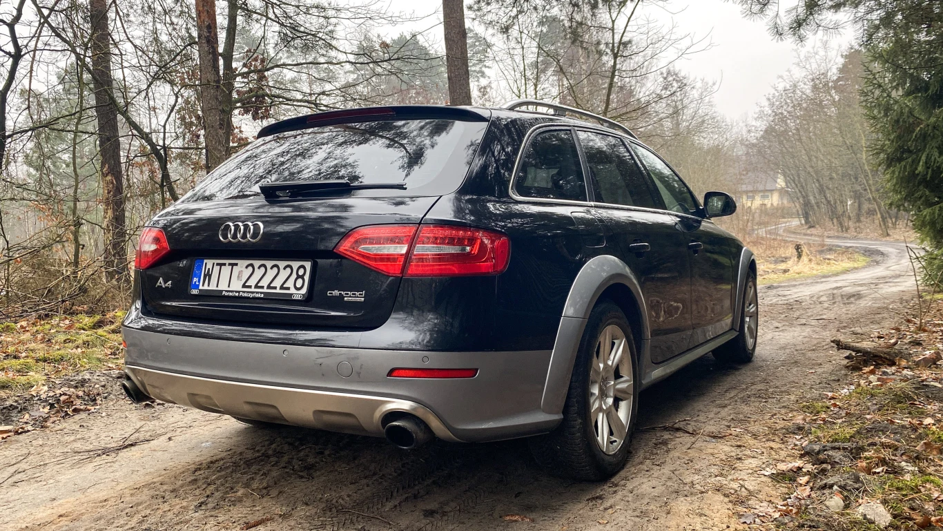 Samochód Audi A4 Allroad zaparkowany na wiejskiej, piaszczystej drodze w otoczeniu drzew i liści.