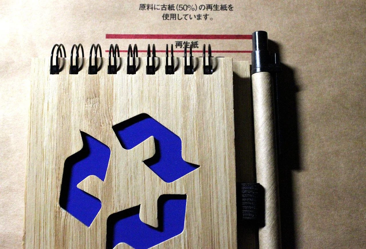 Notes bambusowy z wyciętym symbolem recyklingu, długopisem i tekstem w języku japońskim na tle z ekologicznego papieru.