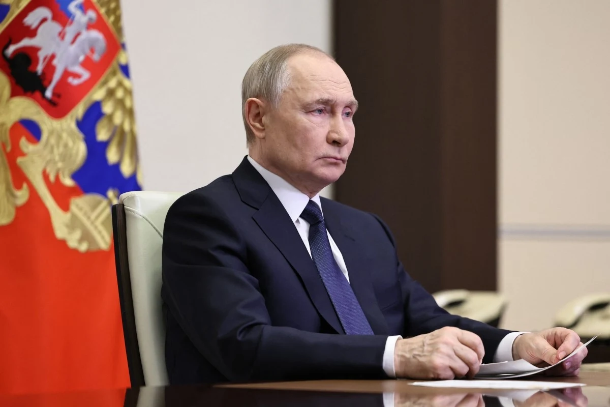 Władimir Putin ogłasza zawieszenie broni Postać mężczyzny w garniturze siedzącego przy stole, w tle fragment flagi z herbem.