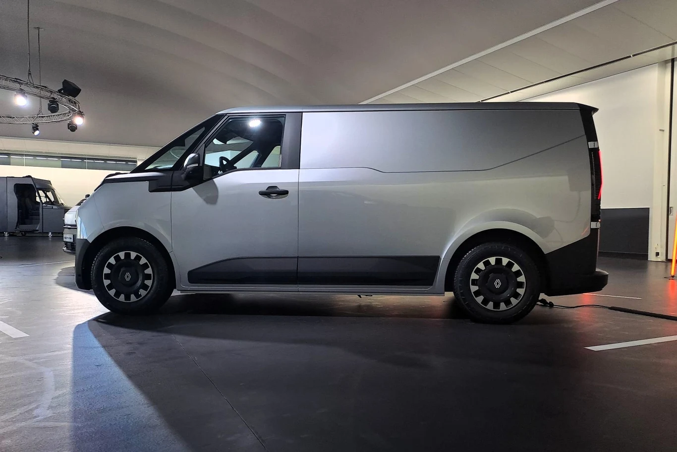 Furgonetka w nowoczesnym stylu, zaparkowana w dobrze oświetlonym pomieszczeniu. Białe nadwozie i czarne akcenty podkreślają elegancki design pojazdu.