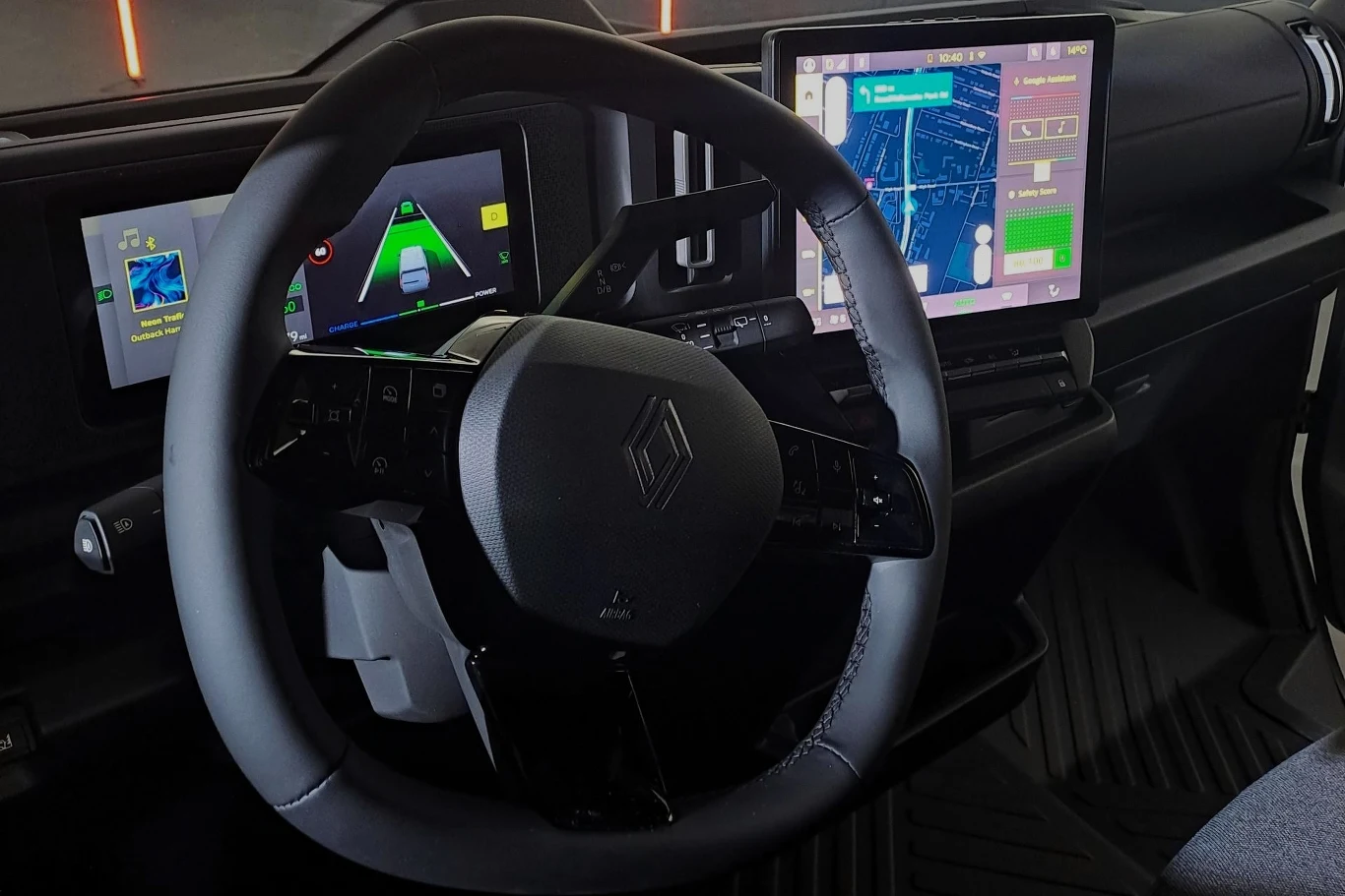 Wnętrze nowoczesnego samochodu elektrycznego z wyświetlaczami cyfrowymi na desce rozdzielczej. Widoczne są kierownica z logotypem producenta oraz duże ekrany dotykowe pokazujące nawigację i informacje dotyczące jazdy.