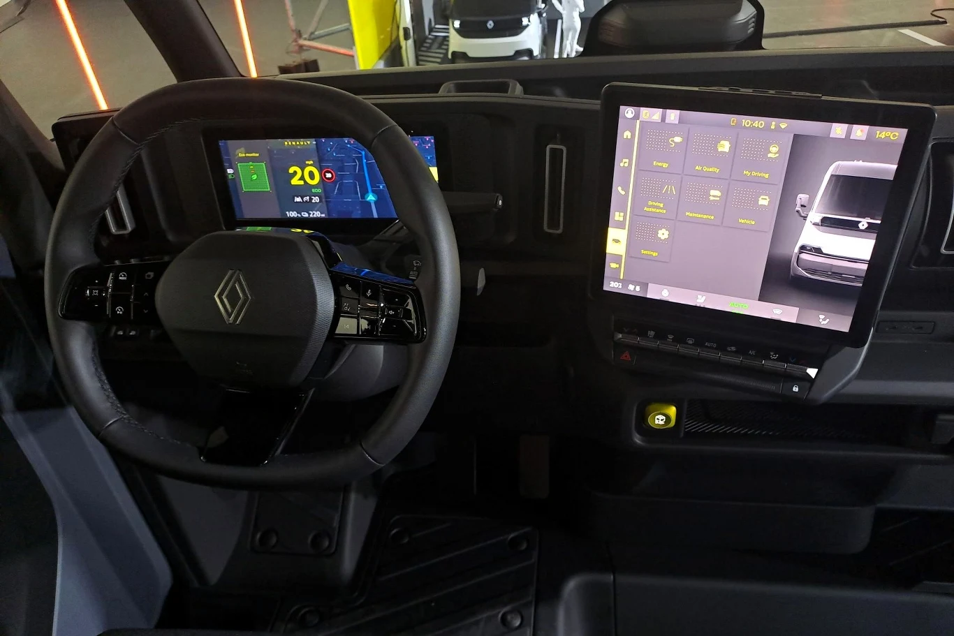 Wnętrze samochodu z nowoczesnymi ekranami dotykowymi, na których widoczne są dane dotyczące jazdy i funkcjonalności pojazdu. Kierownica ma logo producenta, a ekrany pokazują grafikę i ikony związane z obsługą auta.