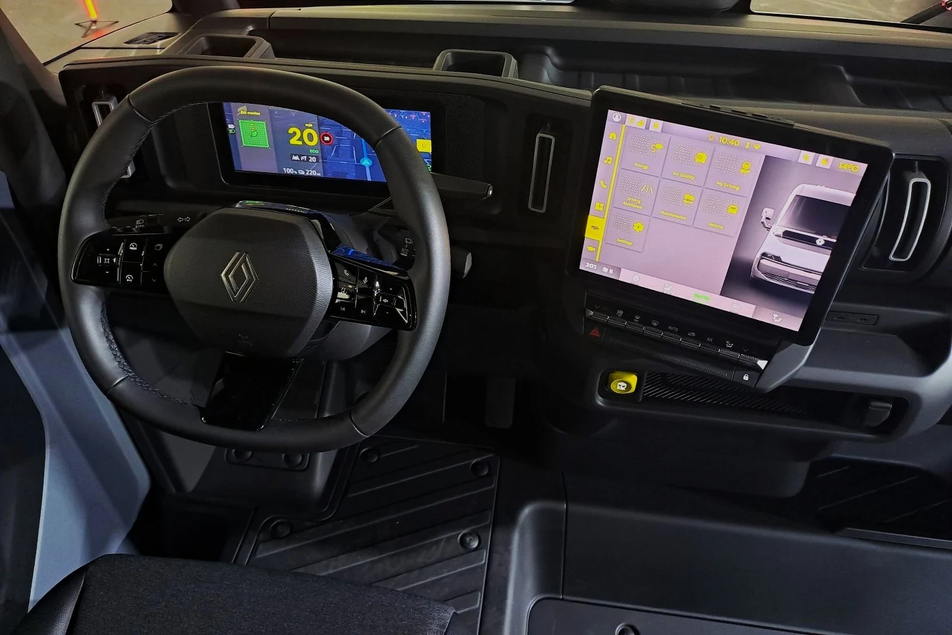 Wnętrze nowoczesnego pojazdu z dużym wyświetlaczem dotykowym po prawej stronie i klasyczną kierownicą. Pulpit nawigacyjny zawiera cyfrowe zegary i wskaźniki. Przestrzeń jest ergonomiczna, zaprojektowana z myślą o wygodzie kierowcy.