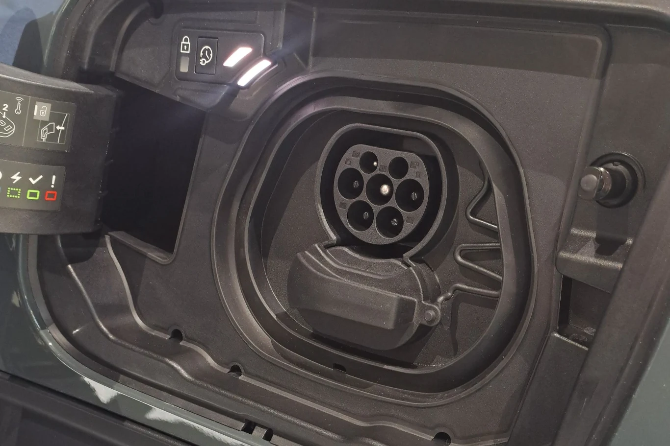 Gniazdo do ładowania samochodu elektrycznego z widocznymi symbolami ładowania i blokady. Wewnątrz oczekuje na podłączenie wtyczki do ładowania.