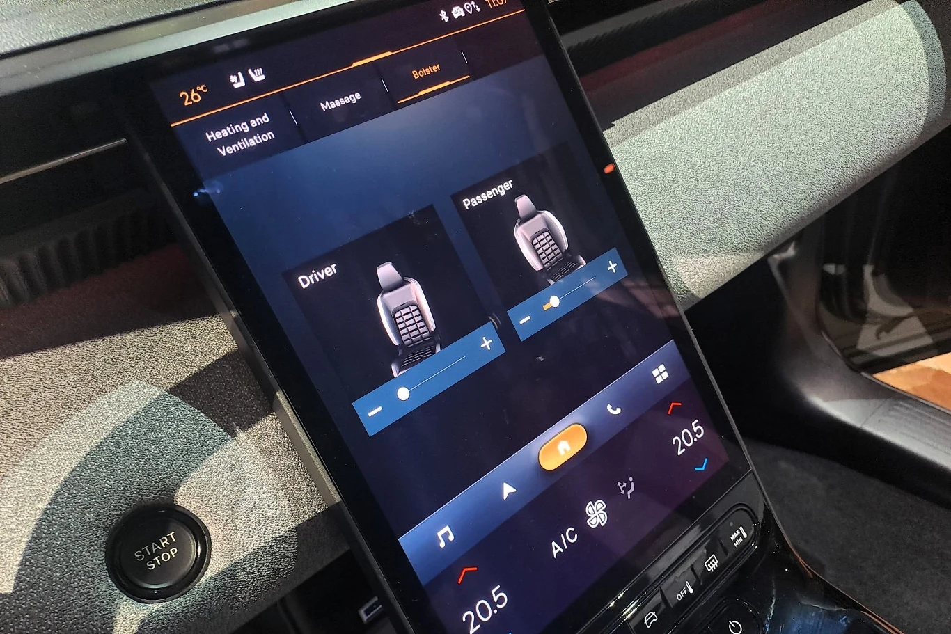 Ekran dotykowy w samochodzie wyświetla interfejs do zarządzania systemem wentylacji i ogrzewania siedzeń. Na ekranie widoczne są ikony przedstawiające siedzenia dla kierowcy i pasażera, z możliwością regulacji ustawień w literkach i symbolach.