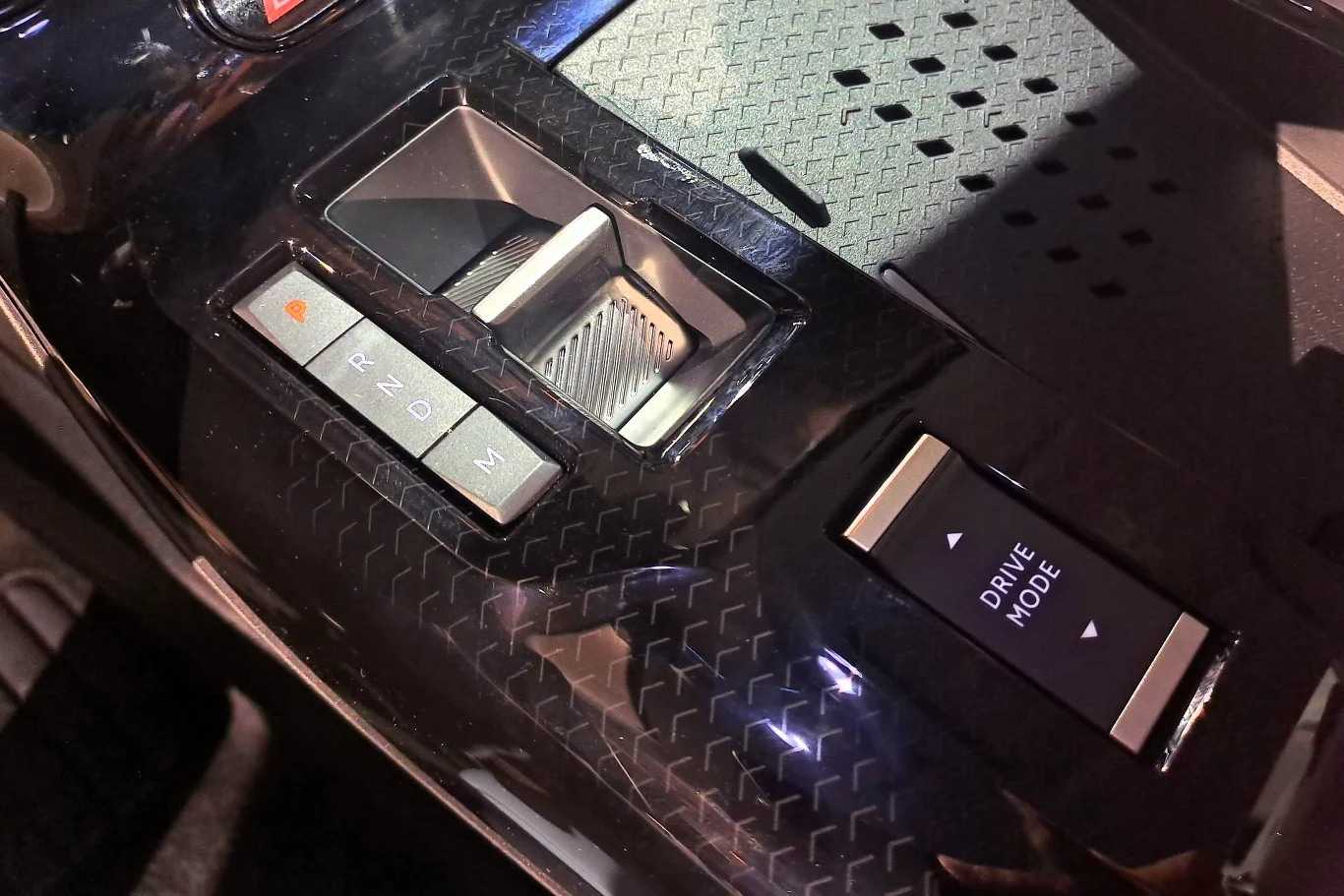 Panel sterowania w luksusowym samochodzie z przyciskami do zmiany trybu jazdy i schowkiem.