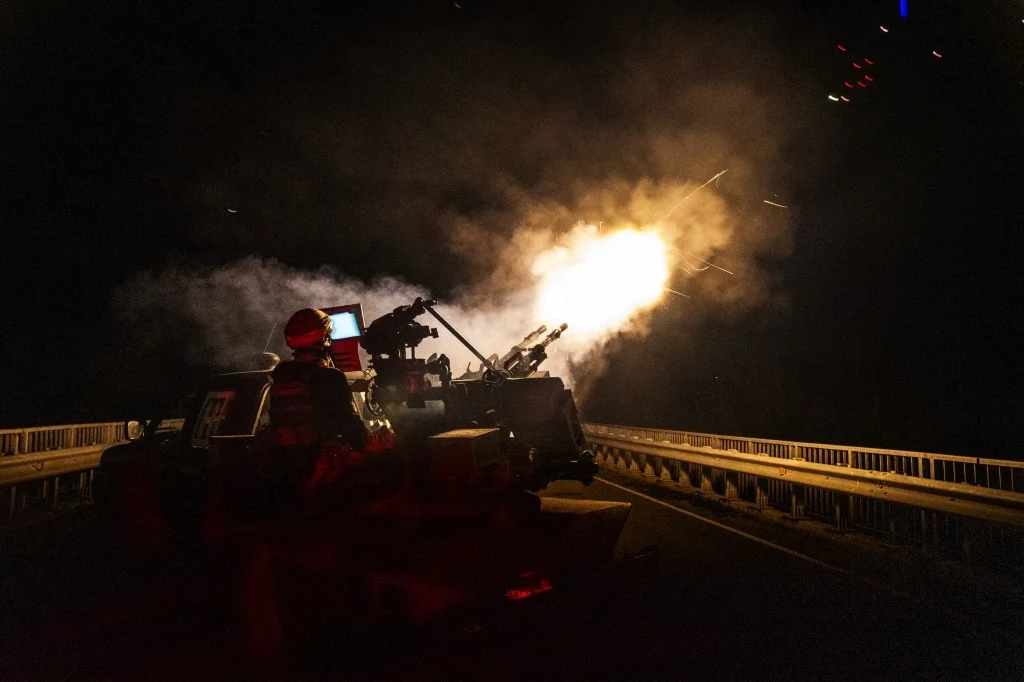 Ukraińska obrona powietrzna w obwodzie łymańskim Scena nocna przedstawiająca wojskowy pojazd, z którego wystrzeliwuje pocisk. Żołnierz w hełmie jest widoczny z tyłu, otoczony dymem i migoczącymi światłami.