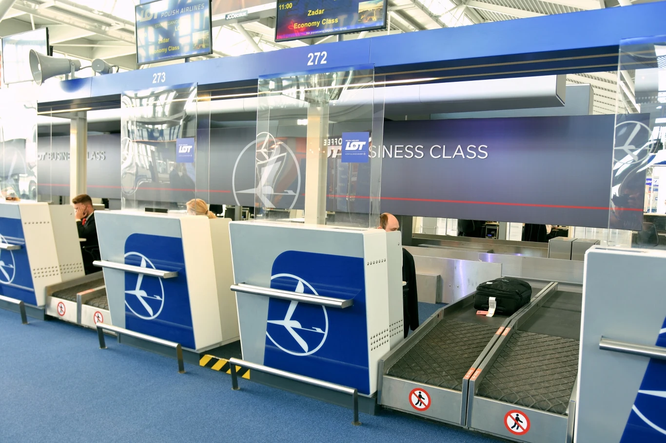 Strefa odprawy biletowo-bagażowej linii lotniczych LOT z numerami stanowisk 272 i 273, z widocznymi taśmociągami do przewozu bagażu i oznaczeniami business class.
