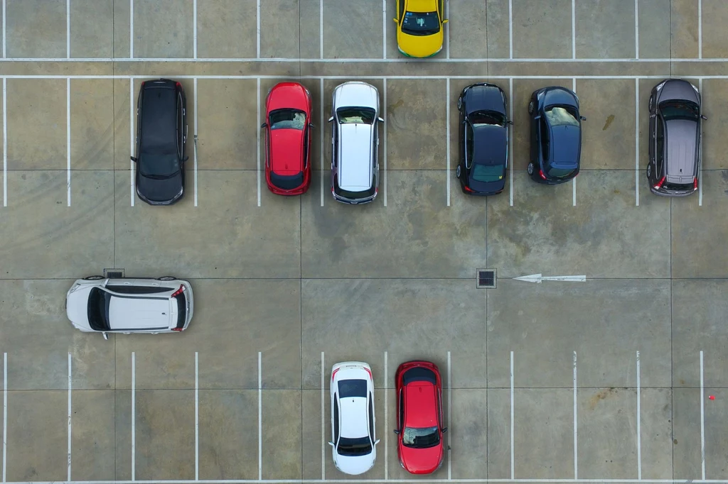 Jak się odnaleźć na parkingach przy popularnych marketach? Widok z lotu ptaka na parking z kilkoma zaparkowanymi samochodami, widoczne podjazdy i linie wyznaczające miejsca parkingowe.