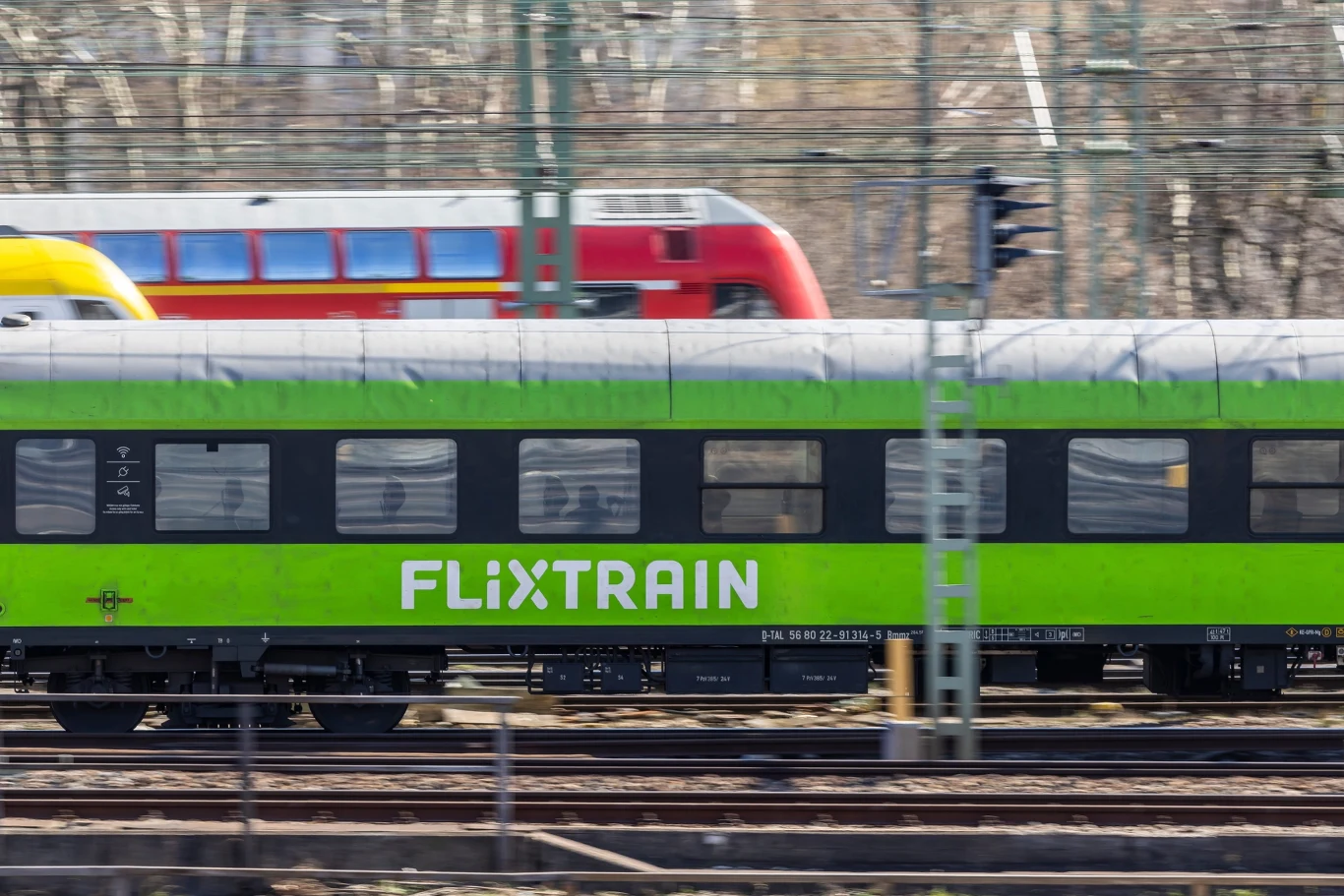 Niemiecki przewoźnik wkracza na kluczową trasę Nowoczesny pociąg FlixTrain w jaskrawym zielonym kolorze poruszający się po torach kolejowych z dużą prędkością. W tle widać inny pociąg w kolorze czerwonym, dalszy plan ukazuje zarysy infrastruktury kolejowej.