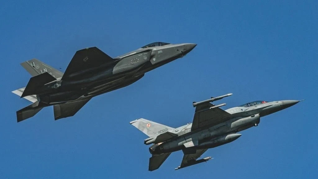 Departament Stanu USA wyraził zgodę na sprzedaż Polsce rakiet powietrze-powietrze AIM-120D Dwa nowoczesne myśliwce wojskowe w locie na niebie. Oba samoloty mają oznaczenia wojskowe na kadłubach, a tło stanowi czyste błękitne niebo. Ujęcie dynamiczne, ukazujące potęgę i technologię lotniczą.
