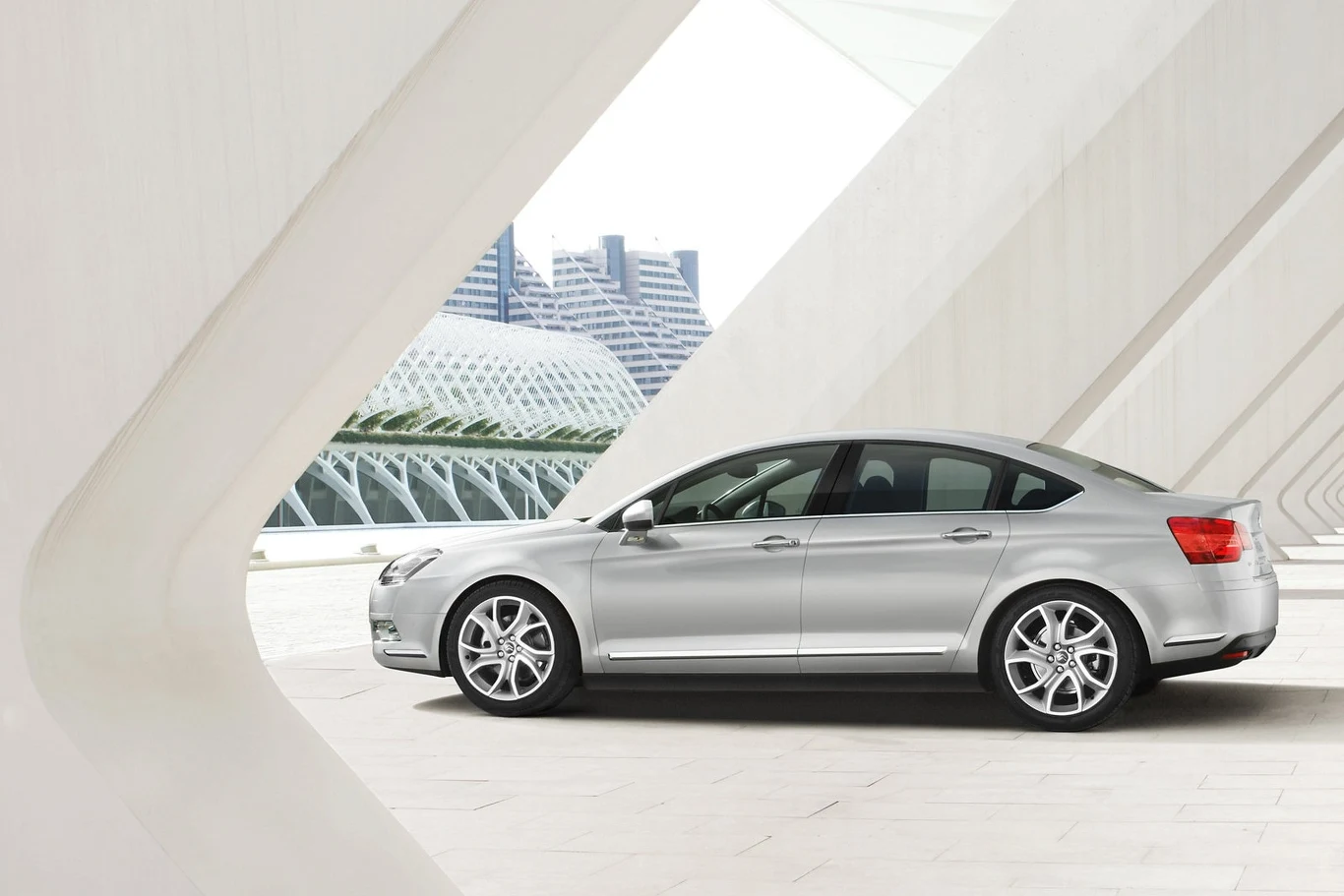 Srebrny samochód osobowy w nowoczesnym otoczeniu architektonicznym z widocznym futurystycznym budynkiem w tle.