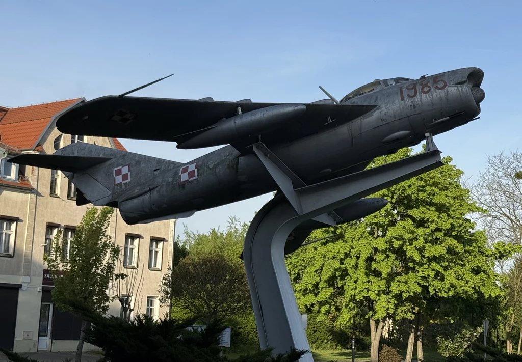 Samolot Lim-5P (MiG-17PF), którym latał Mirosław Hermaszewski, do dziś jest atrakcją Wołowa. Samolot myśliwski na postumencie otoczony zielenią, w tle budynek mieszkalny. Konstrukcja prezentuje się na tle błękitnego nieba.