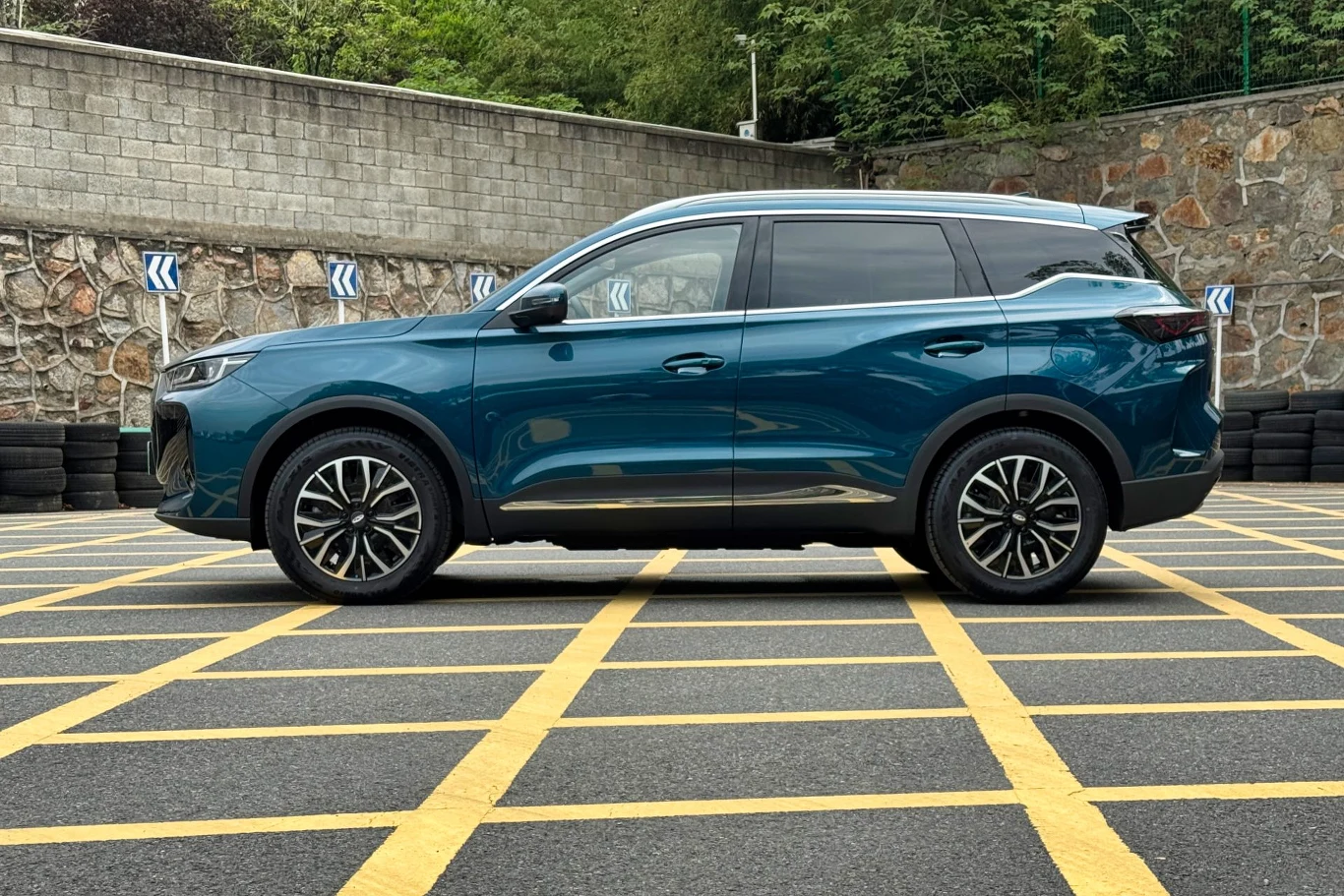 Nowoczesny SUV o eleganckim designie w kolorze niebieskim zaparkowany na oznakowanym parkingu, w otoczeniu murów i zieleni, z wyraźnym układem kół i świateł.