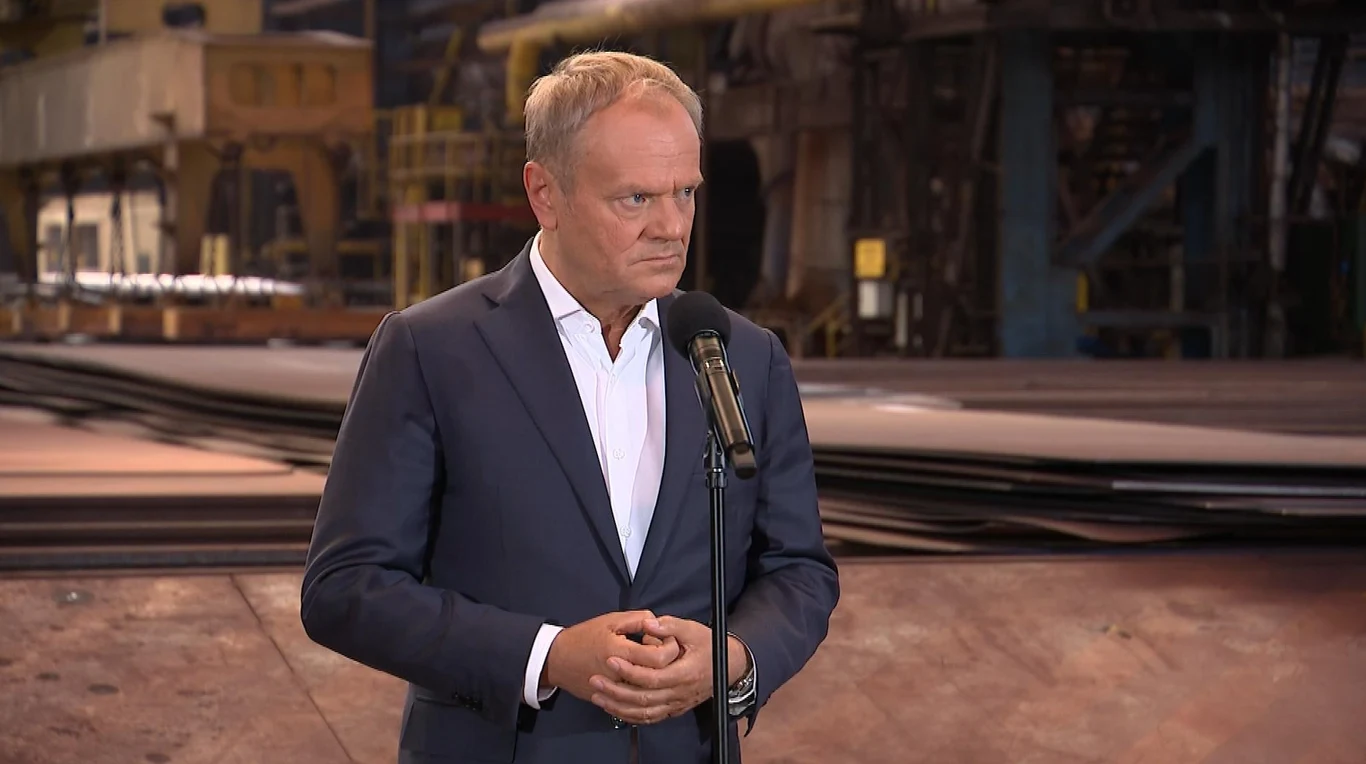 Premier Donald Tusk poinformował o dymisja szefa Służby Więziennej Mężczyzna w garniturze stoi przed mikrofonem w fabrycznej hali, kompletnie skoncentrowany na przemowie.