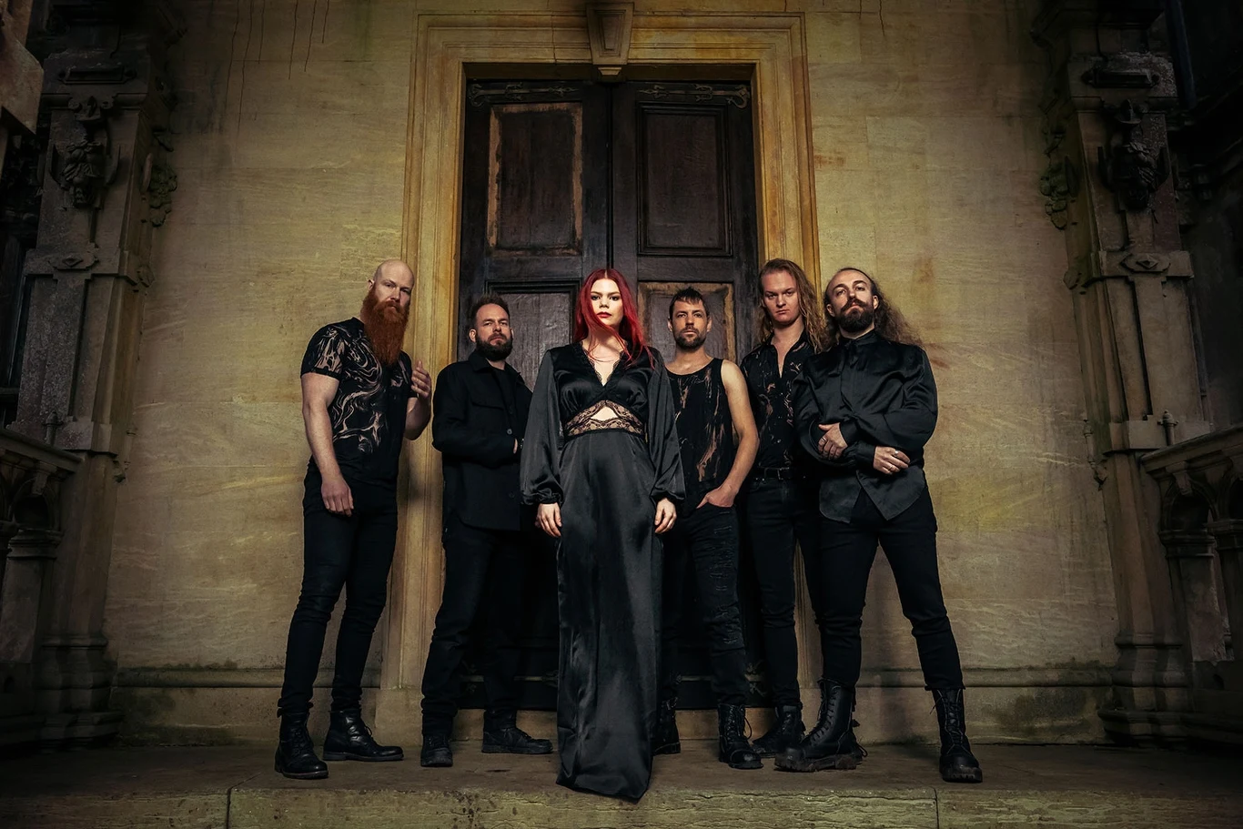 Blackbriar szykuje nowy album Grupa sześciu osób ubranych w czarne, gotyckie ubrania pozuje przed masywnymi, drewnianymi drzwiami na tle architektonicznego detalu w stylu gotyckim. Centralna postać to kobieta z długimi, czerwonymi włosami, otoczona przez pięciu mężczyzn.