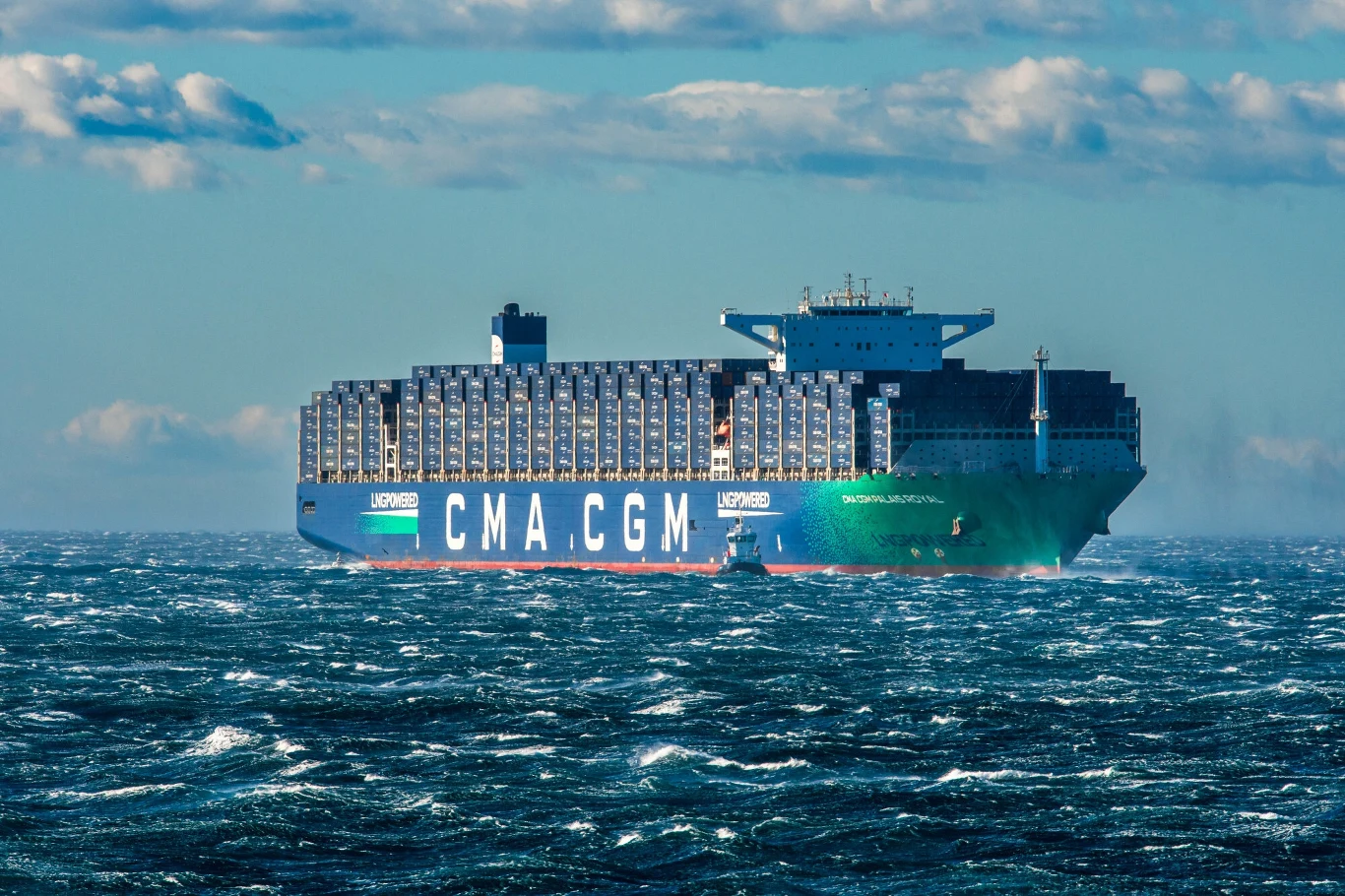 Kontenerowiec CMA CGM płynie przez fale na otwartym morzu, niebo jest częściowo zachmurzone.