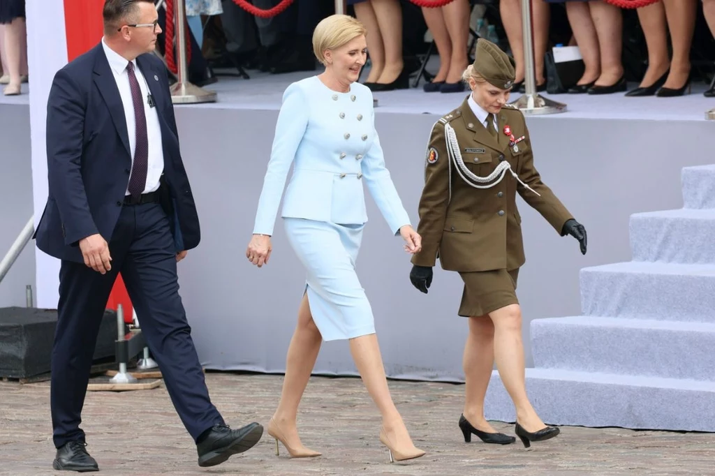 Agata Kornhauser-Duda podczas obchodów Święta Konstytucji Trzeciego Maja Osoby ubrane elegancko i w mundur wojskowy idą po schodach na tle publiczności.