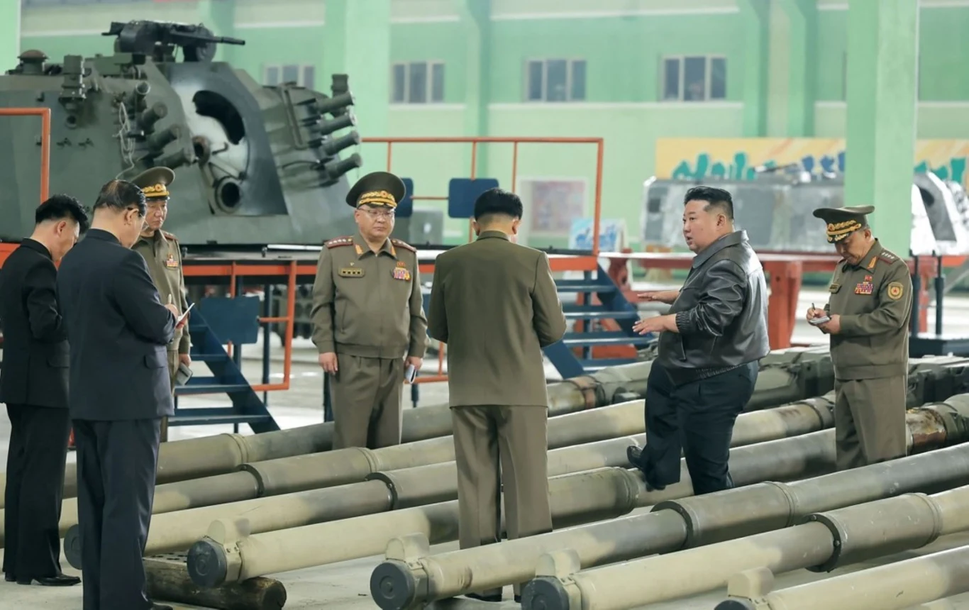 Kim Dzong Un dokonał inspekcji w jednej z fabryk sprzętu wojskowego Grupa mężczyzn w mundurach wojskowych stoi wokół dużych elementów sprzętu wojskowego w hali fabrycznej. Lider, w czarnej kurtce, zdaje się coś omawiać z innymi uczestnikami spotkania.