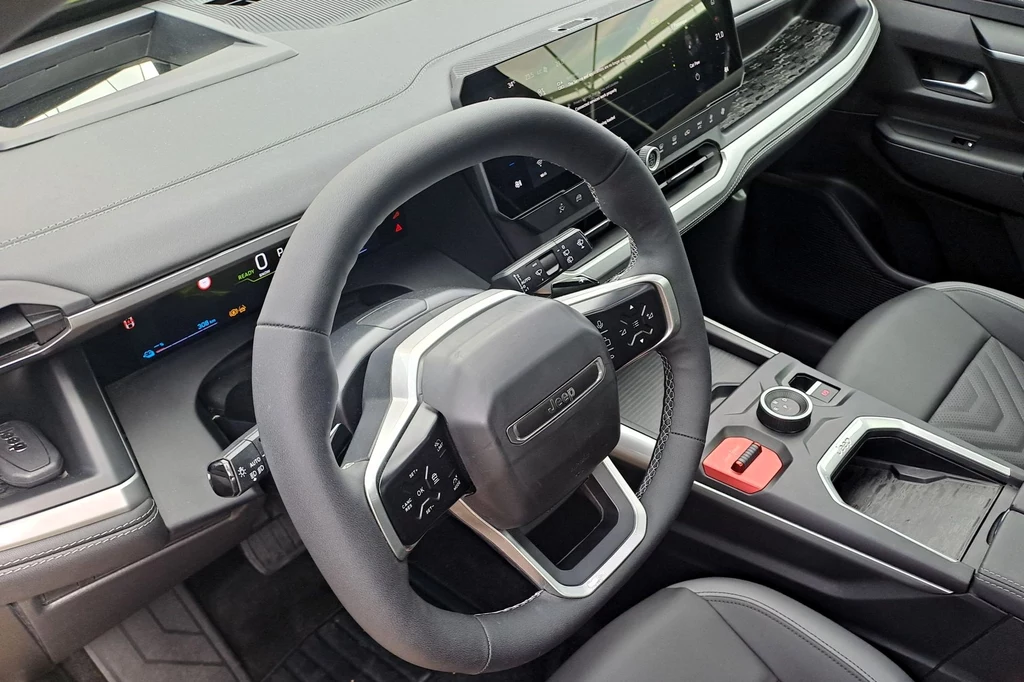 Jeep Compass wyposażony jest w 10-calowy ekran wskaźników i 16-calowy wyświetlacz multimediów. Wnętrze samochodu z widokiem na elegancki kokpit i kierownicę. Dominuje czarne wykończenie oraz nowoczesny design. Centralnym punktem jest duży ekran dotykowy, a całość aranżacji jest starannie zaprojektowana z myślą o komforcie kierowcy.
