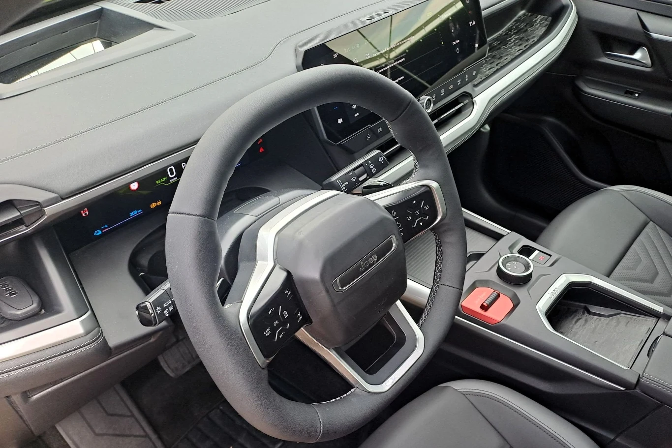 Wnętrze samochodu z widokiem na elegancki kokpit i kierownicę. Dominuje czarne wykończenie oraz nowoczesny design. Centralnym punktem jest duży ekran dotykowy, a całość aranżacji jest starannie zaprojektowana z myślą o komforcie kierowcy.